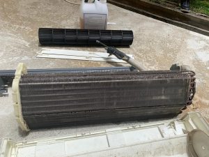 A close-up of a technician removing heavily clogged mesh filters to address an air conditioner not cooling issue in a residential home in Singapore