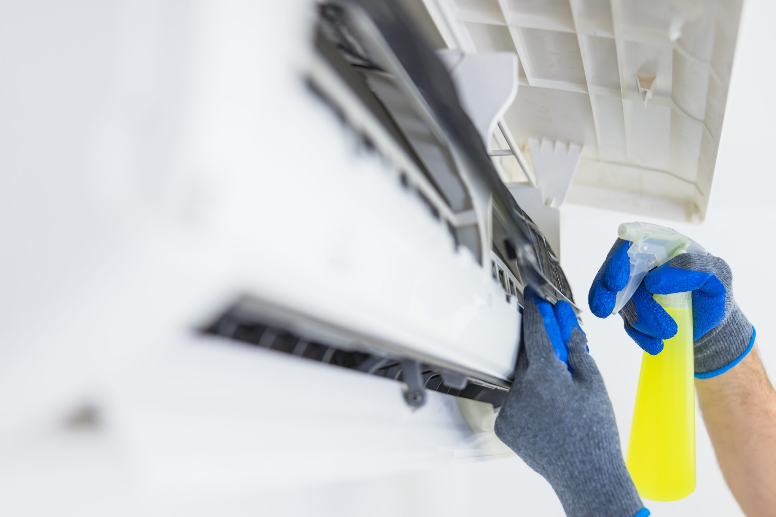 A professional technician in safety gloves performing an aircon chemical wash Singapore by spraying a specialized cleaning solution onto indoor coils