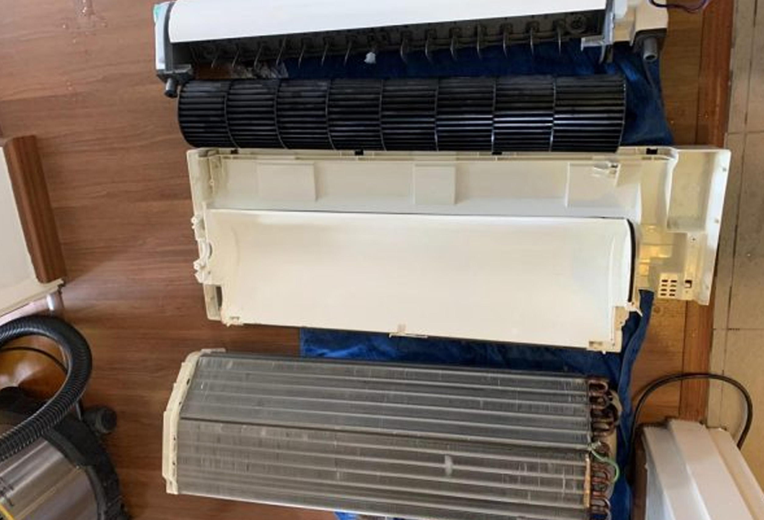 Dismantled air conditioner indoor unit showing blower fan and evaporator coil for cleaning