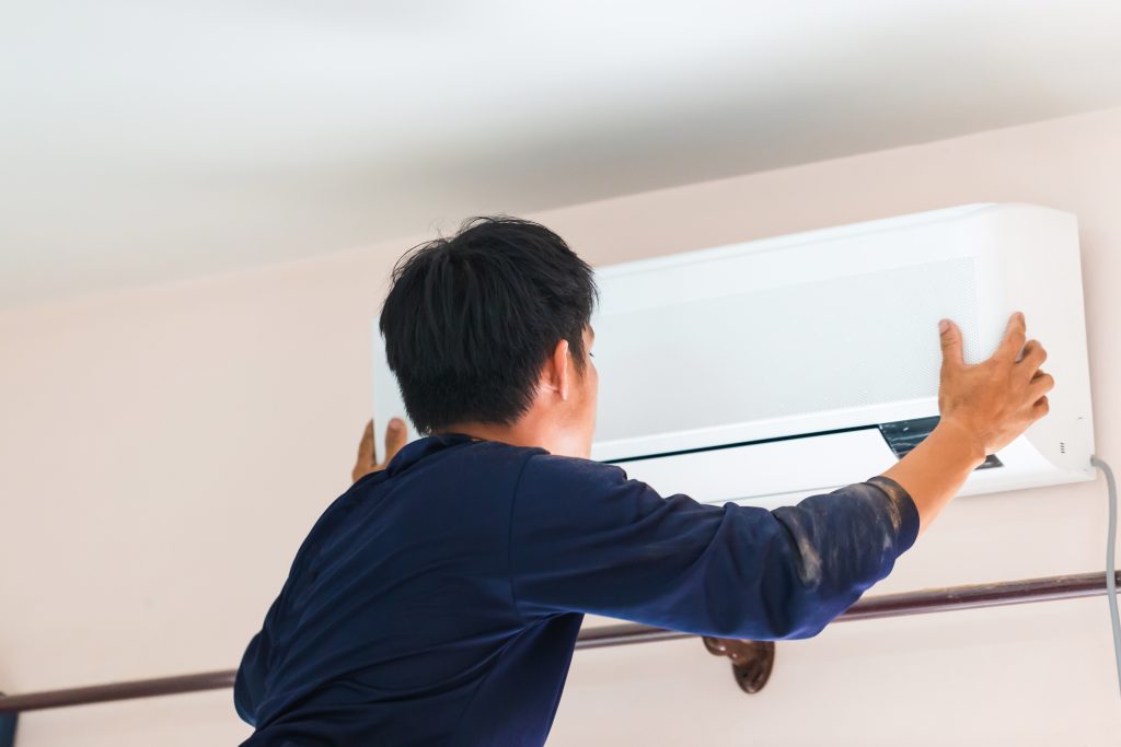Professional technician in a dark blue shirt carefully inspecting or mounting a white wall-mounted aircon unit