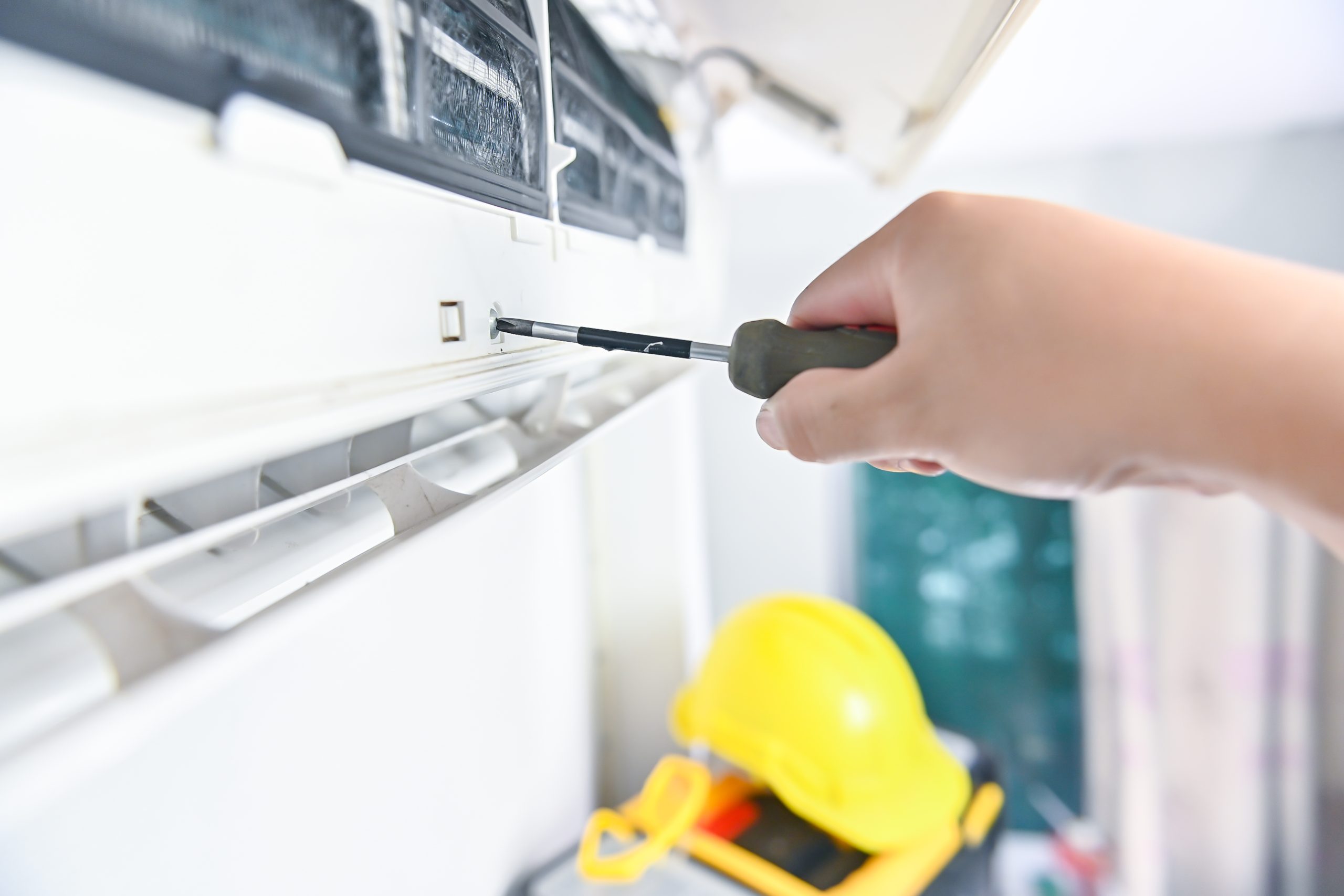A hand using a manual screwdriver to tighten or remove a screw from the plastic casing of an indoor aircon unit